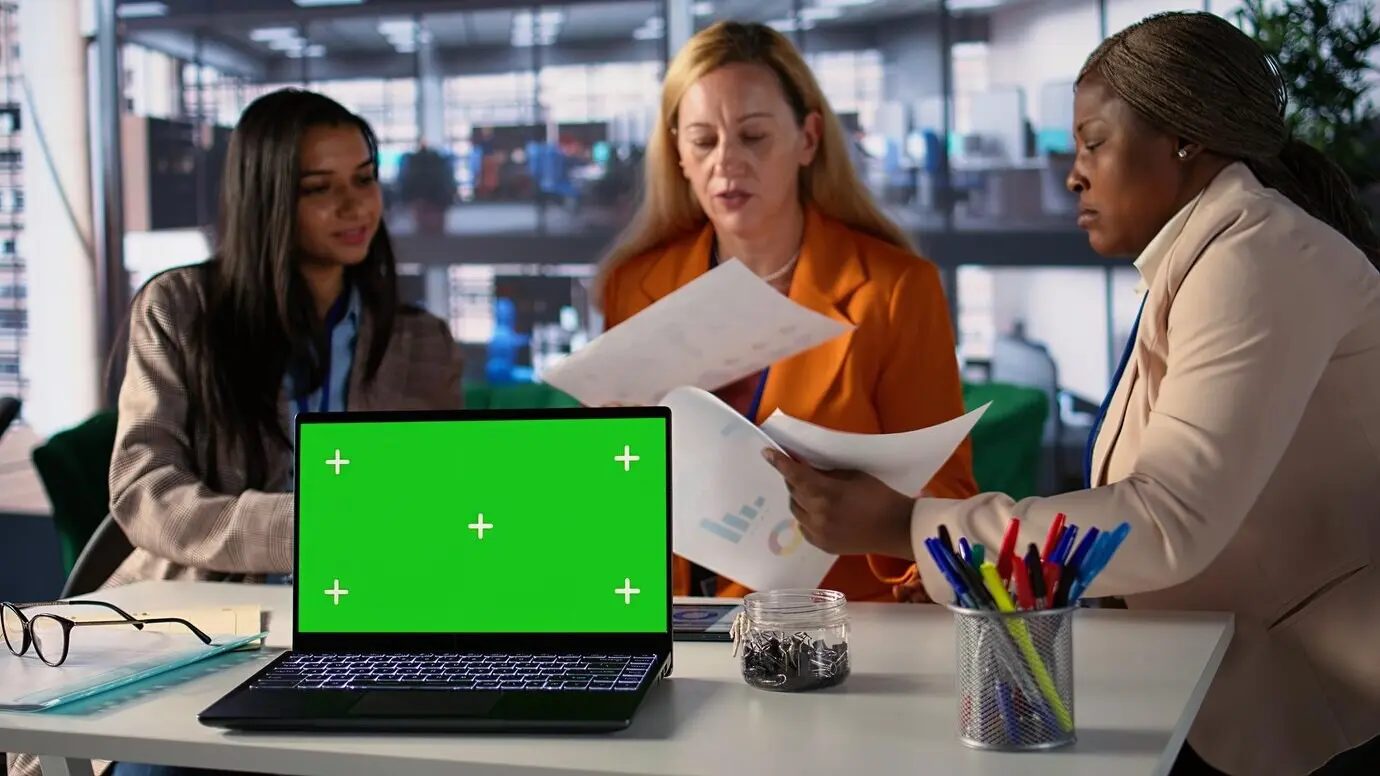 Деловые женщины разных этнических групп работают рядом с изолированным зеленым экраном.